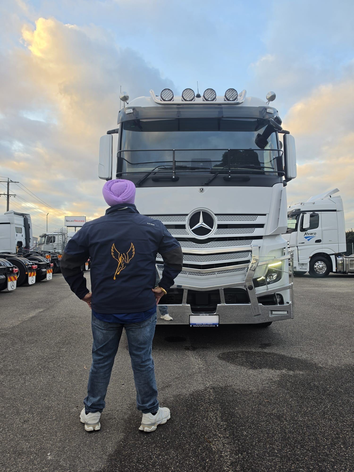 Flying Horse driver in a Pegasus jacket facing a Mercedes-Benz Actros in the yard