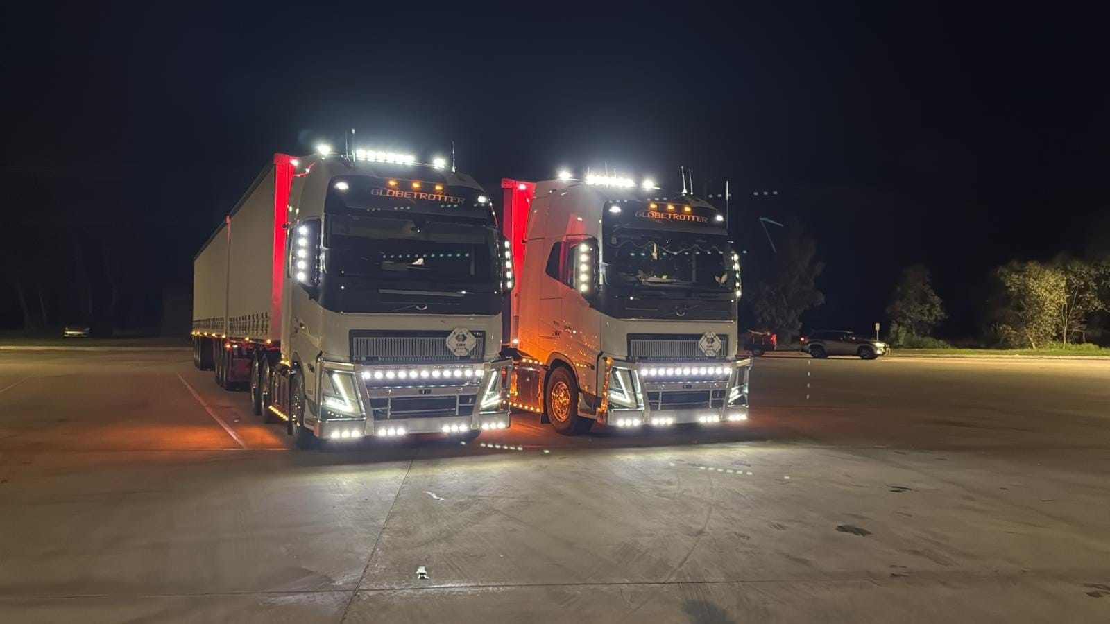 Two Flying Horse Volvo prime movers with their lights on, lined up for a night departure